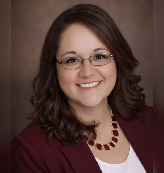 Smiling woman with glasses and a burgundy necklace.